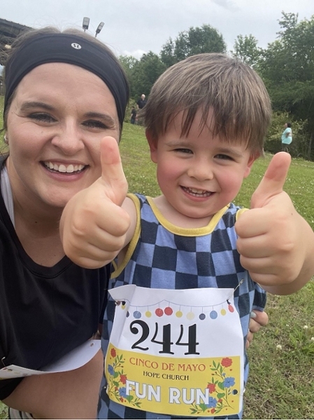 A woman smiling with child giving two thumbs up.